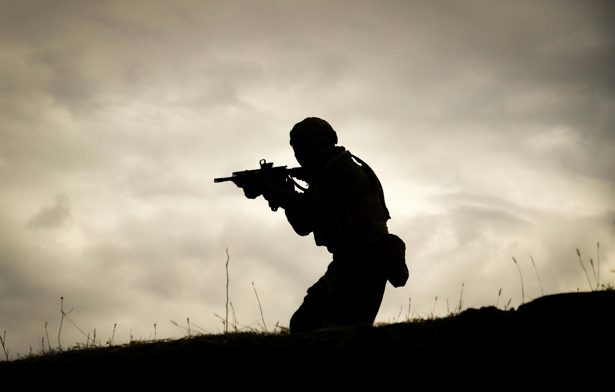 A silhouette of a soldier holding a rifle against a dramatic sunset sky.